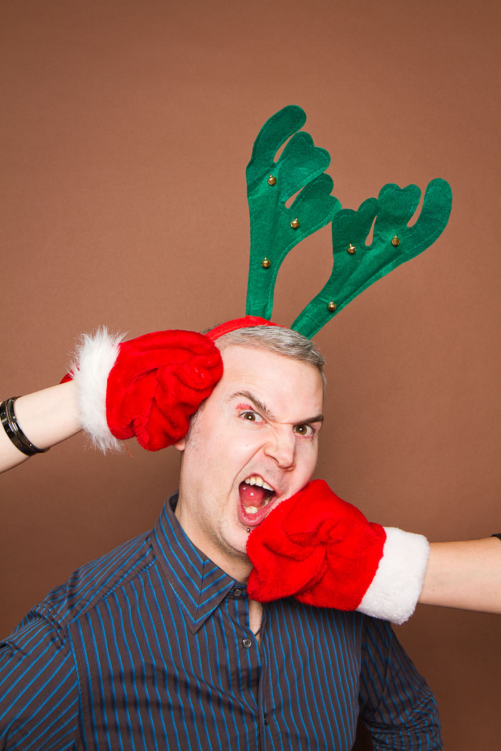 A man in Christmas reindeer antlers gets punched on both sides of his head in funny portrait