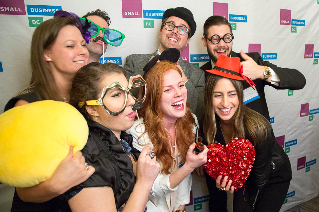 A group of young entrepreneurs pose with silly props in front of a media wall