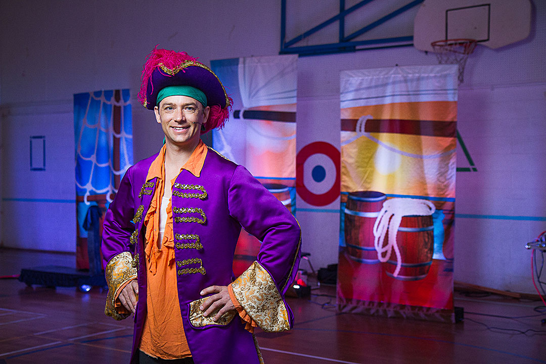 Dustin Anderson, The Purple Pirate stands in front of his set in a school gymnasium